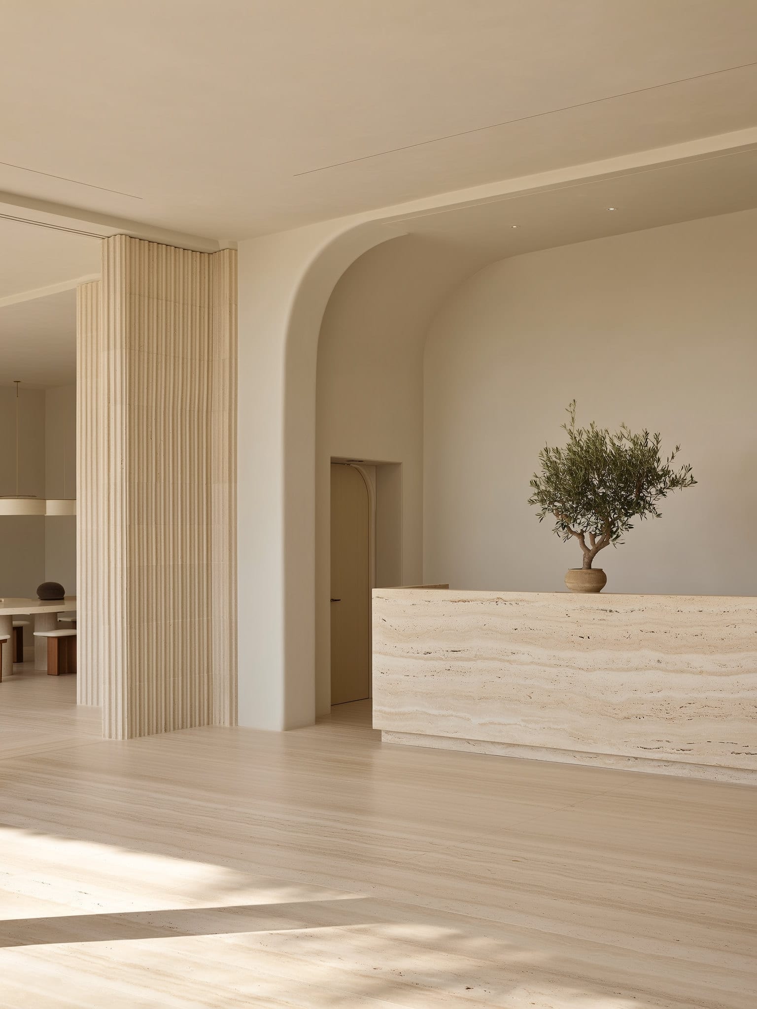 BAYTE studio reception with a travertine desk, an olive tree, and a warm open workspace beyond